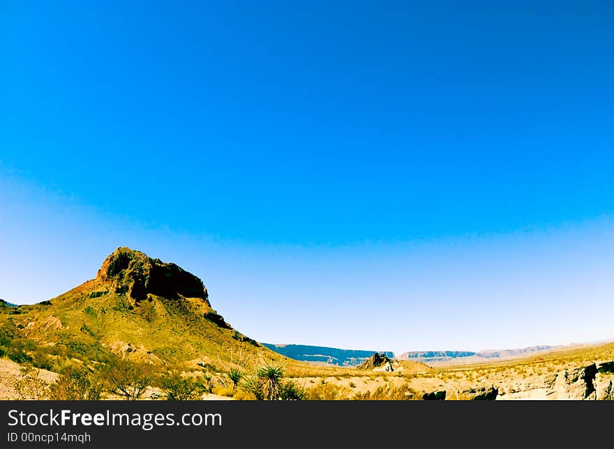 A rock formation reaching into a beautiful, bright, blue expanse of sky.