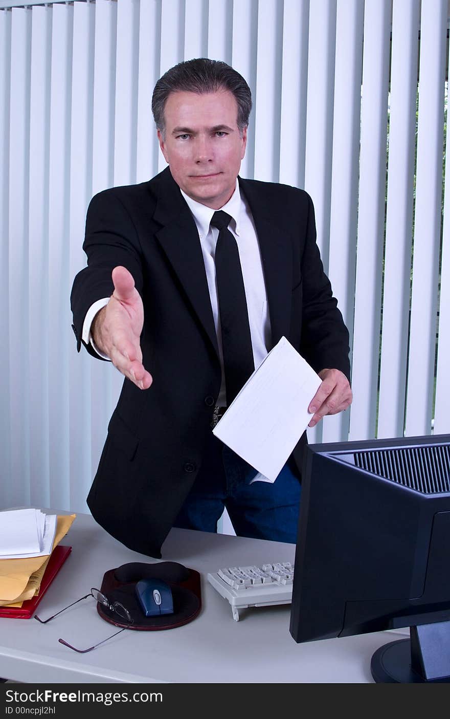 A man standing in front of a desk with his hand extended as if to greet someone. A man standing in front of a desk with his hand extended as if to greet someone.