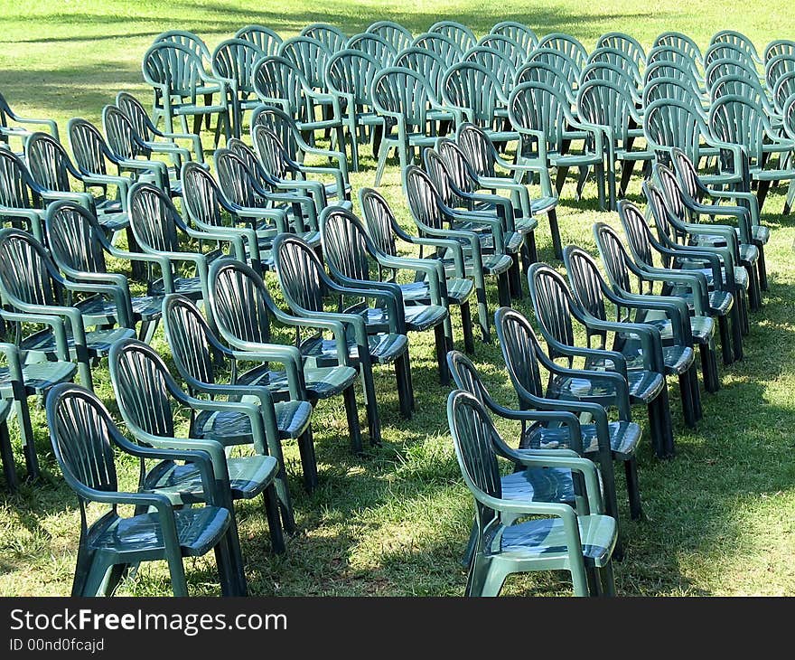 Ranks of empty green plastic outdoor chairs arrayed on lawn in full sunlight. Ranks of empty green plastic outdoor chairs arrayed on lawn in full sunlight