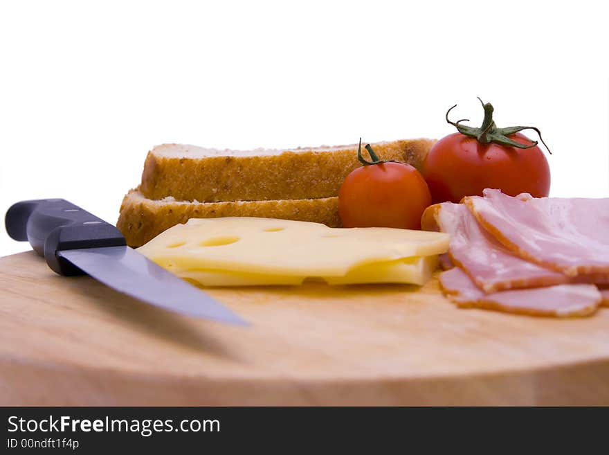 A cutting board with sandwich ingredients (swiss cheese, bacon, tomatoes, bread) and a knife. A cutting board with sandwich ingredients (swiss cheese, bacon, tomatoes, bread) and a knife.