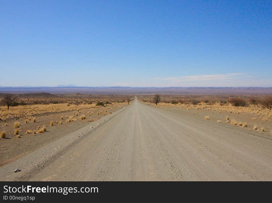 Straight endless gravel road through the namibian desert