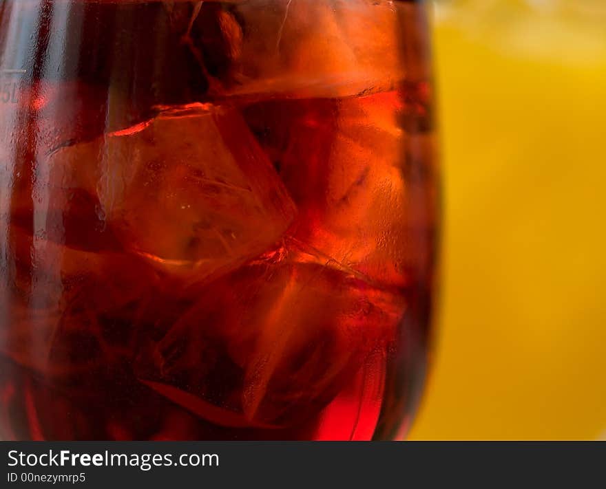 Abstract of ice cubes floating in a backlighted glass of fruit juice against another glass of orange juice. Abstract of ice cubes floating in a backlighted glass of fruit juice against another glass of orange juice