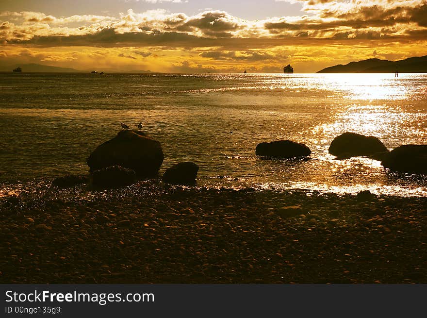 Seagulls perched on rocks watch a glowing sunset over the horizon. Seagulls perched on rocks watch a glowing sunset over the horizon.