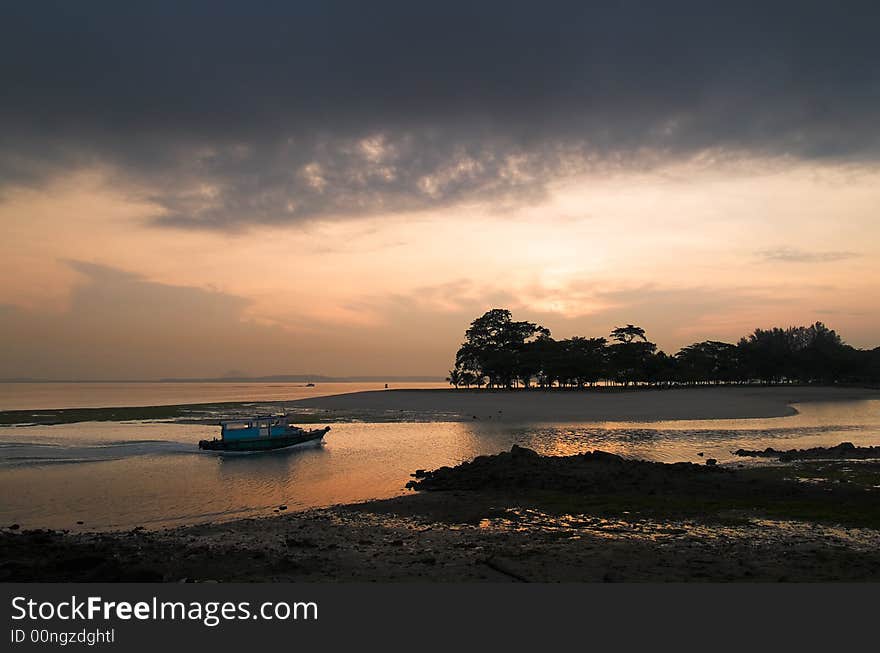 A ferry entering the mouth of a creek at low tide as the sun rises in an overcast sky behind the trees on the far shore. A ferry entering the mouth of a creek at low tide as the sun rises in an overcast sky behind the trees on the far shore.