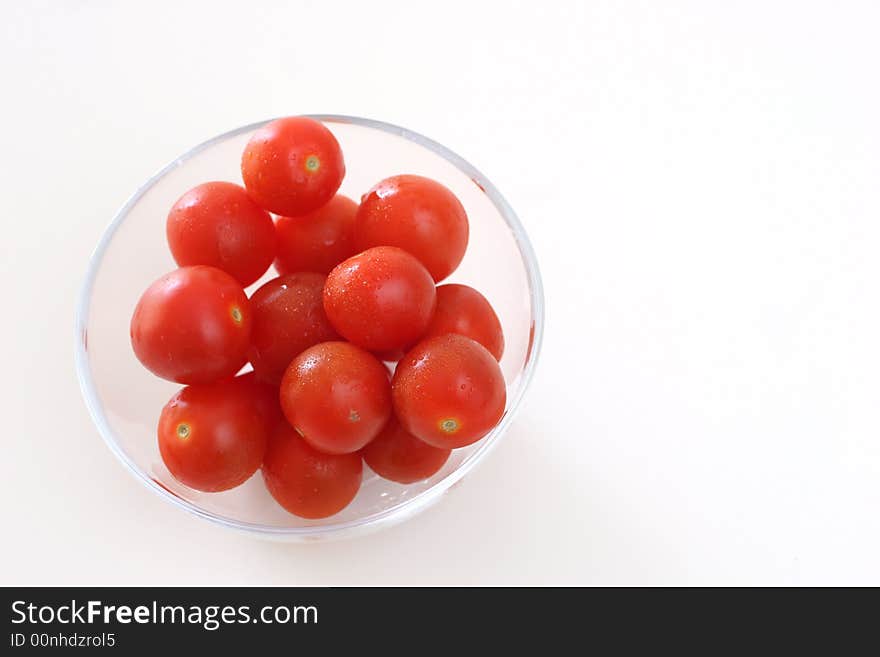 Cherry tomatoes in a transparent glass bowl on a white table-top