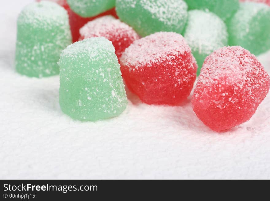 A close up of red and green spiced gumdrops covered in snow. A close up of red and green spiced gumdrops covered in snow.