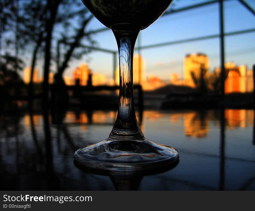 A glass of wine on the table reflecting the buildings at the sunset. A glass of wine on the table reflecting the buildings at the sunset.