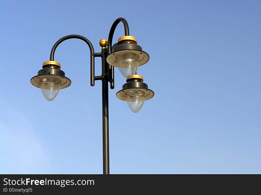 Three ornate street lamps on a lamp post against a blue sky in Romania