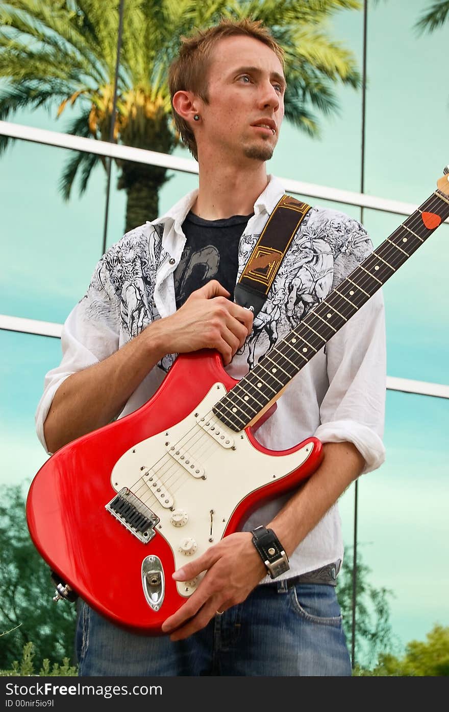 A young man proudly holds his red guitar. A young man proudly holds his red guitar.