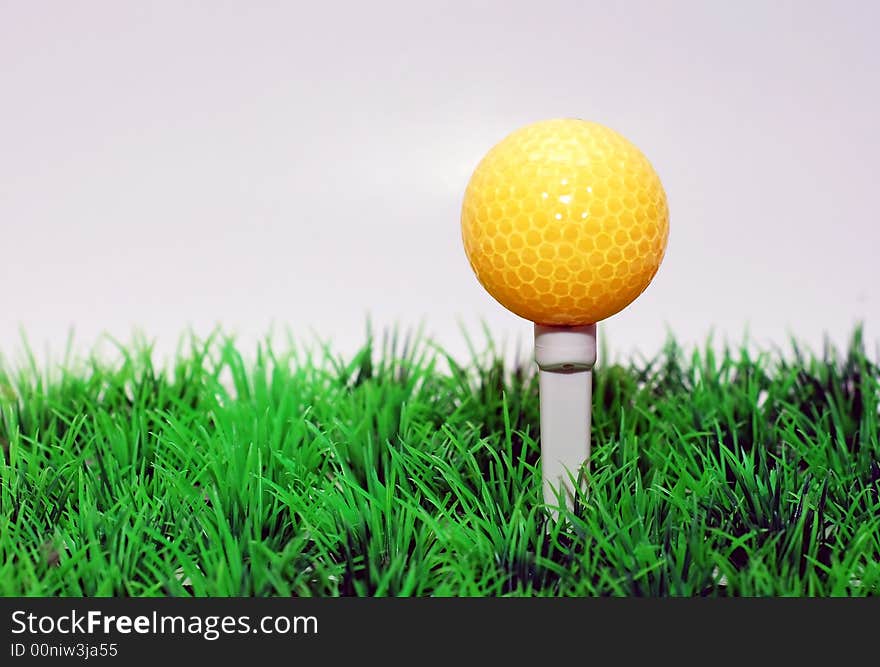 Yellow golfball in orange tee, green fairway, isolated on black background. Yellow golfball in orange tee, green fairway, isolated on black background