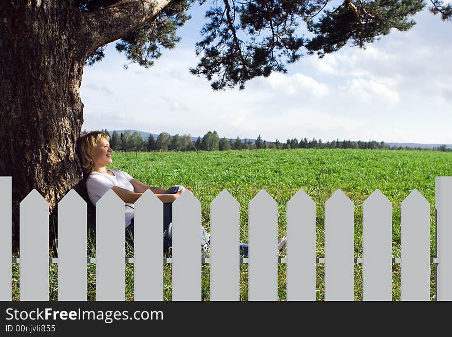 Young beauty woman sit under alone tree in field under blue sky and clouds