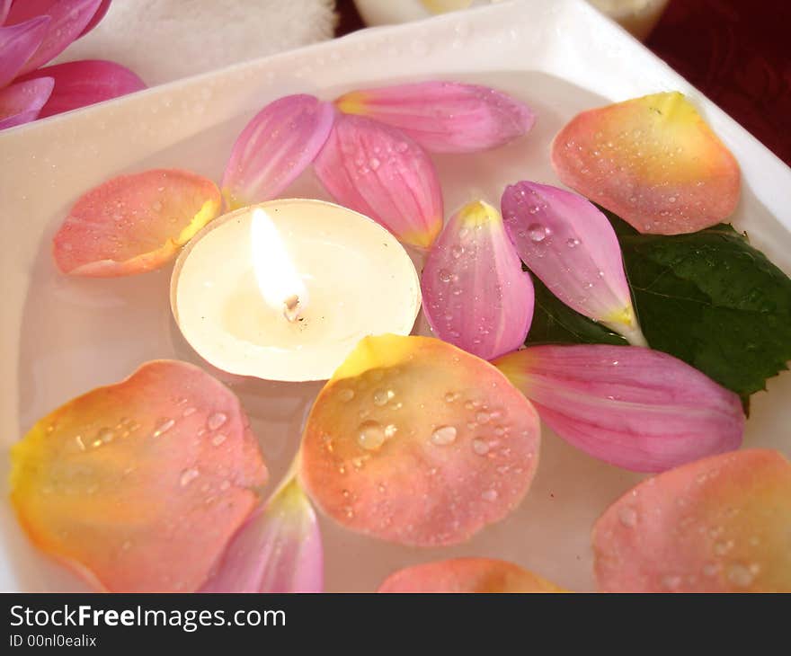 Candle with petals of flowers on water