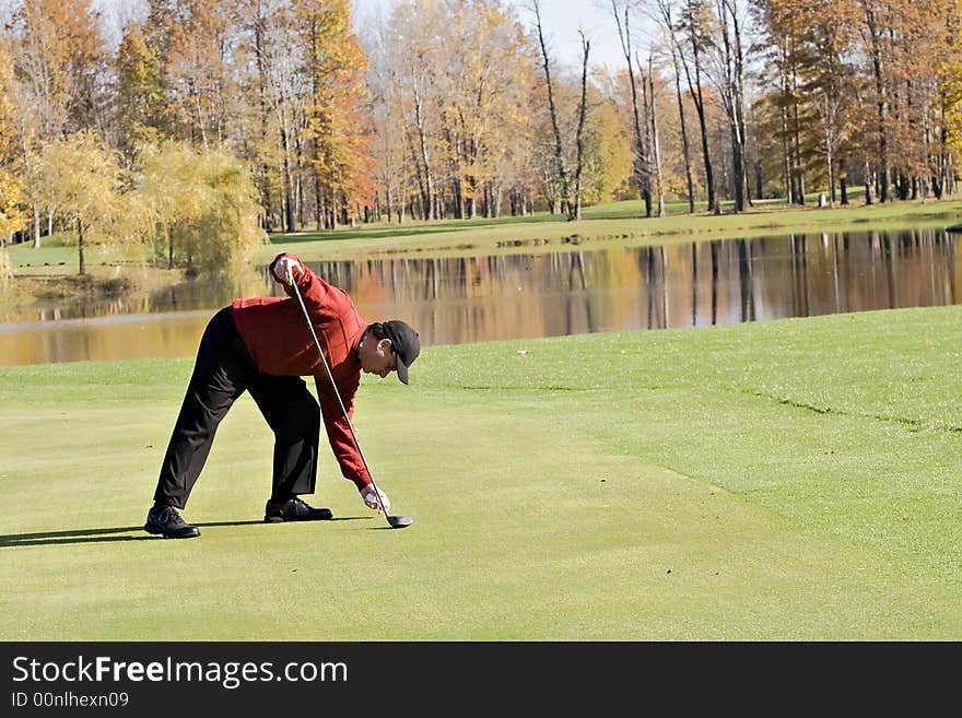 Male Golfer in sweater tees up the ball for a golf shot - Autumn setting. Male Golfer in sweater tees up the ball for a golf shot - Autumn setting