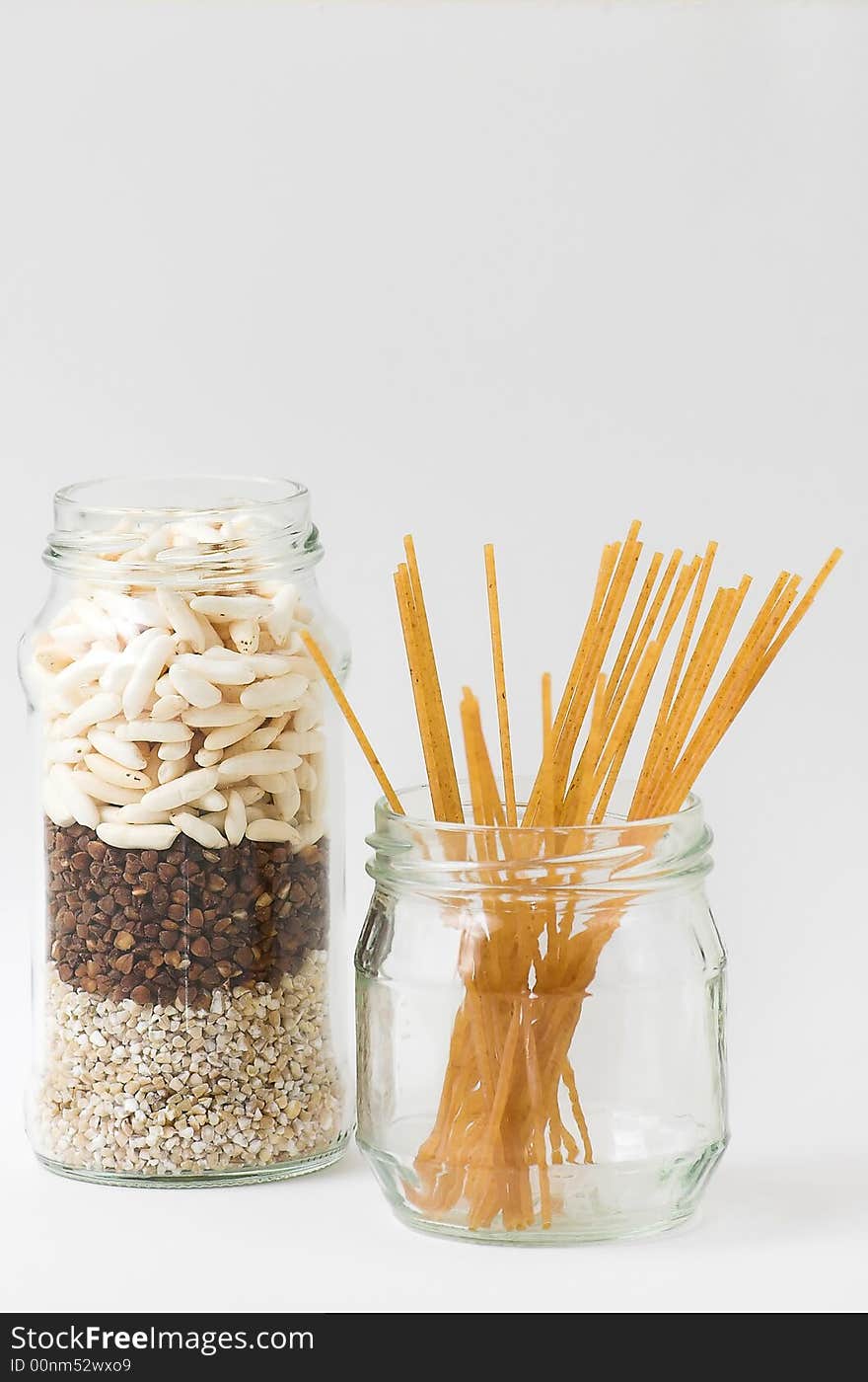 Two glass jars, isolated, filled with three kinds of grain and spaghetti. Two glass jars, isolated, filled with three kinds of grain and spaghetti