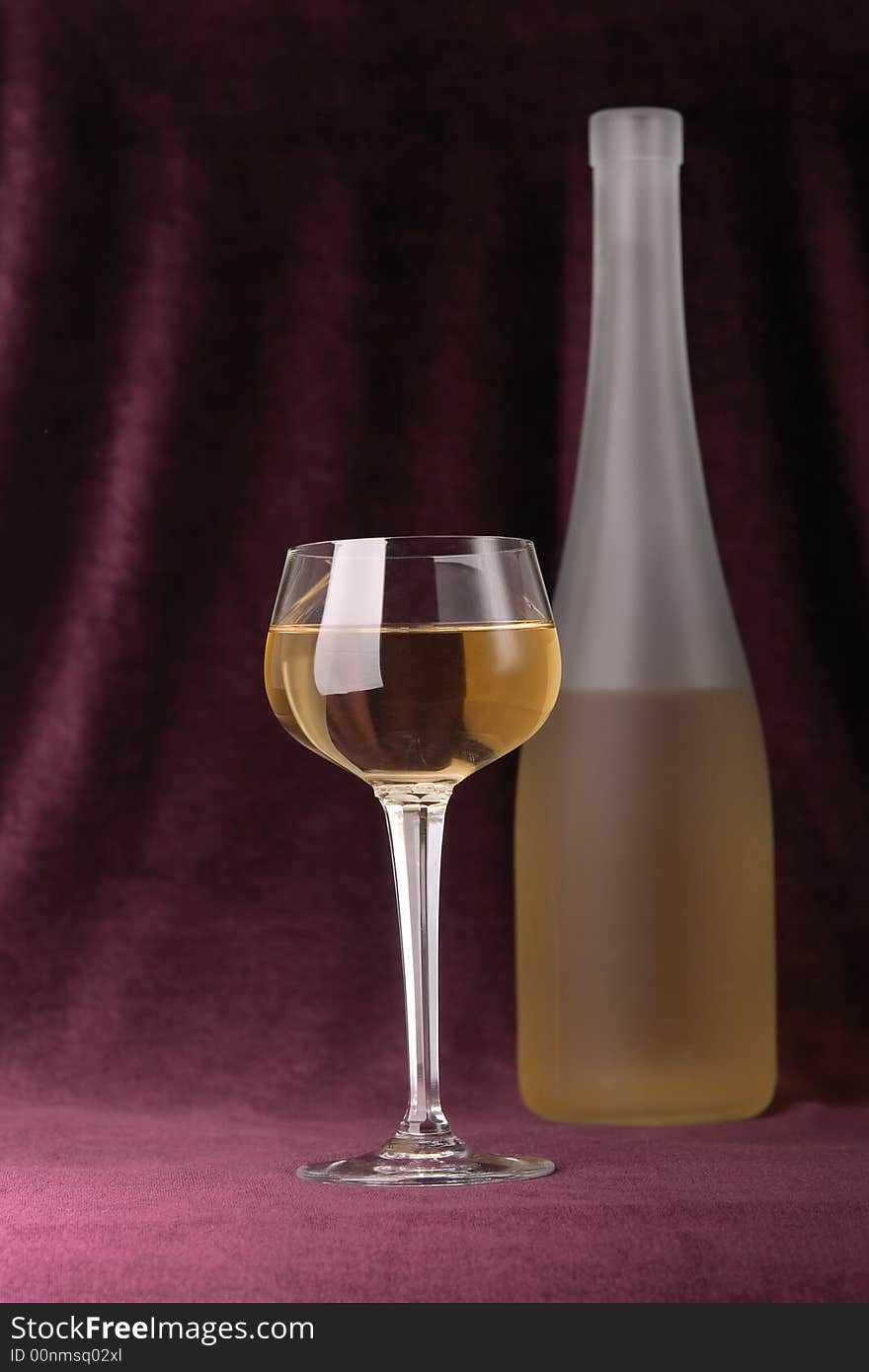 Glass and bottle of white wine on a background of an elegant velveteen material of claret color