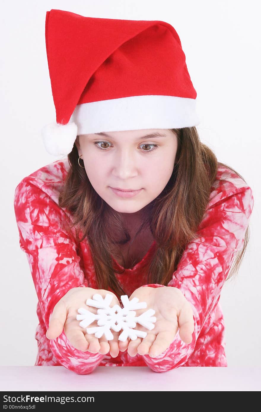 A portrait of a young teenager wearing a red Santa hat and red print top, holds out a large white snowflake in both hands in this studio setting. White background. A portrait of a young teenager wearing a red Santa hat and red print top, holds out a large white snowflake in both hands in this studio setting. White background.