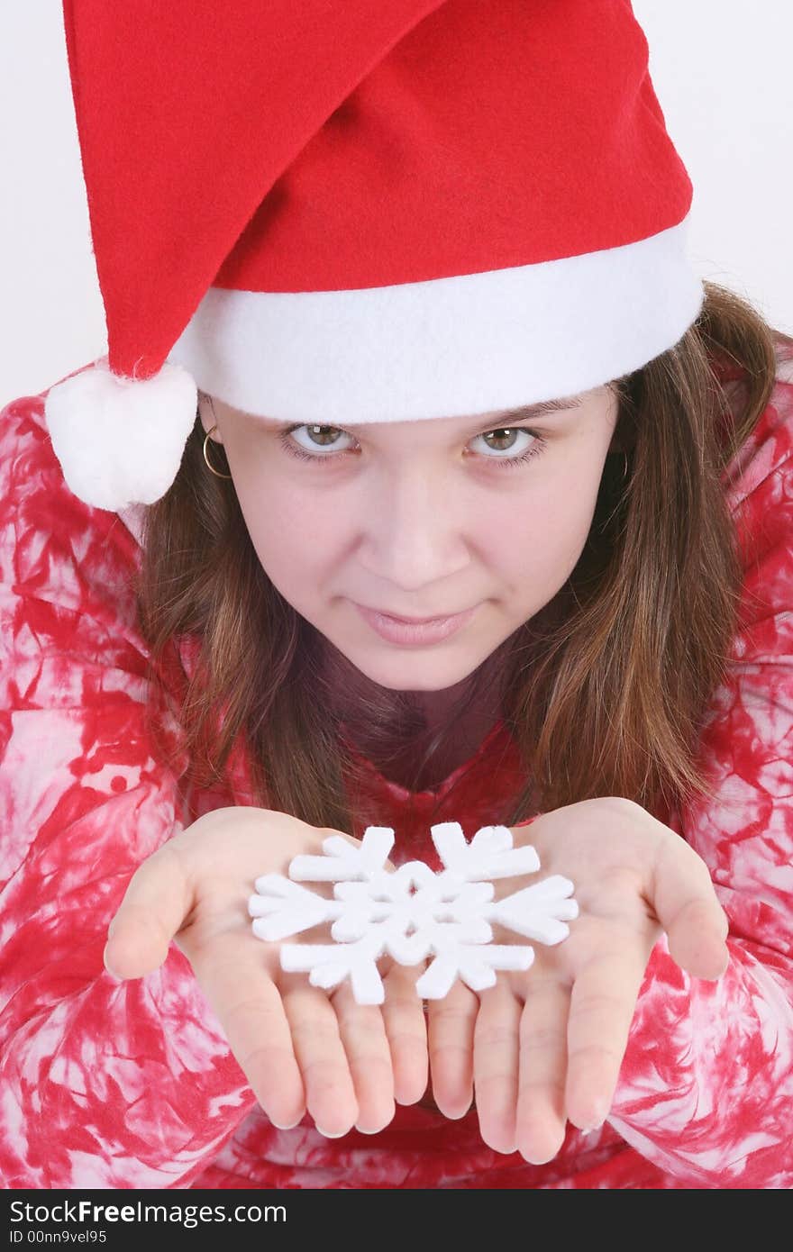 A portrait of a young teenager wearing a red Santa hat and red print top, holds out a large white snowflake in both hands in this studio setting. White background. A portrait of a young teenager wearing a red Santa hat and red print top, holds out a large white snowflake in both hands in this studio setting. White background.