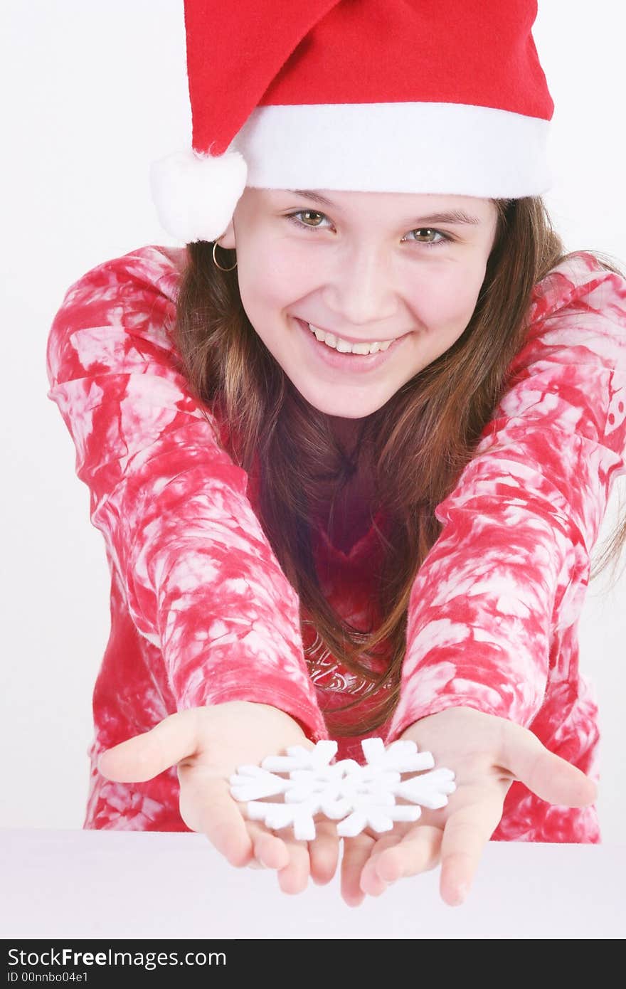 A portrait of a young teenager wearing a red Santa hat and red print top, holds out a large white snowflake in both hands in this studio setting. White background. A portrait of a young teenager wearing a red Santa hat and red print top, holds out a large white snowflake in both hands in this studio setting. White background.