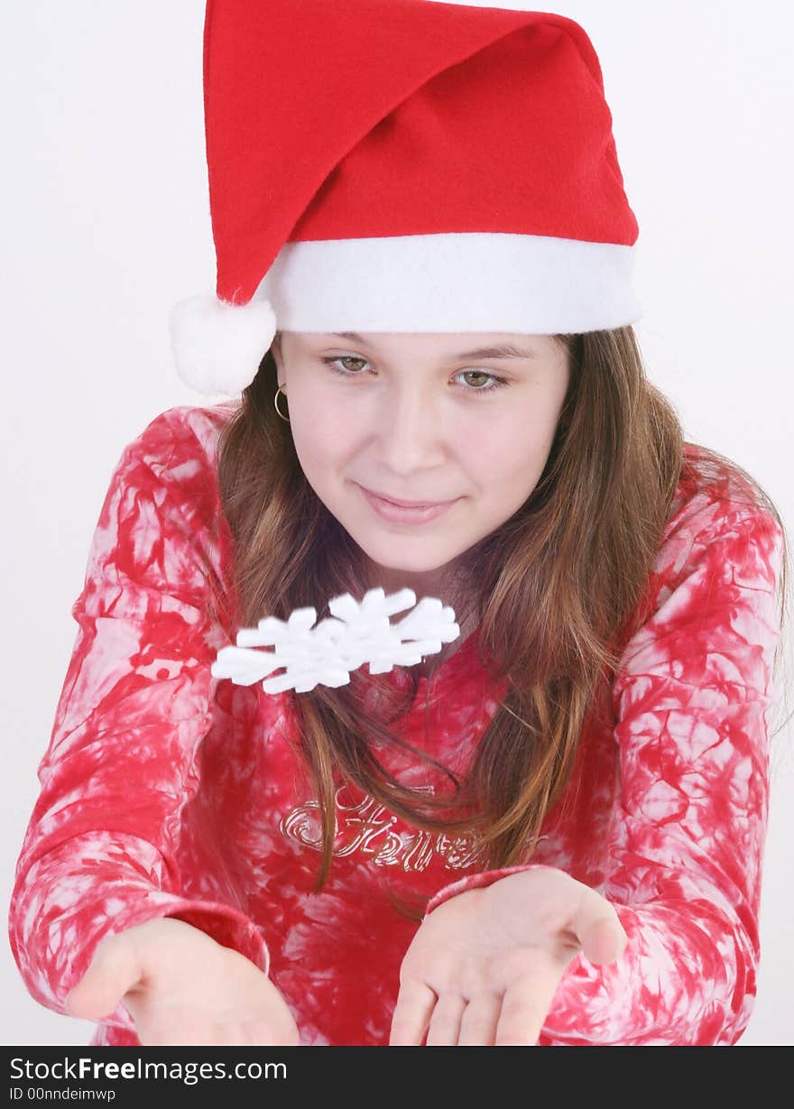 A portrait of a young teenager wearing a red Santa hat and red print top, holds out a large white snowflake in both hands in this studio setting. White background. A portrait of a young teenager wearing a red Santa hat and red print top, holds out a large white snowflake in both hands in this studio setting. White background.