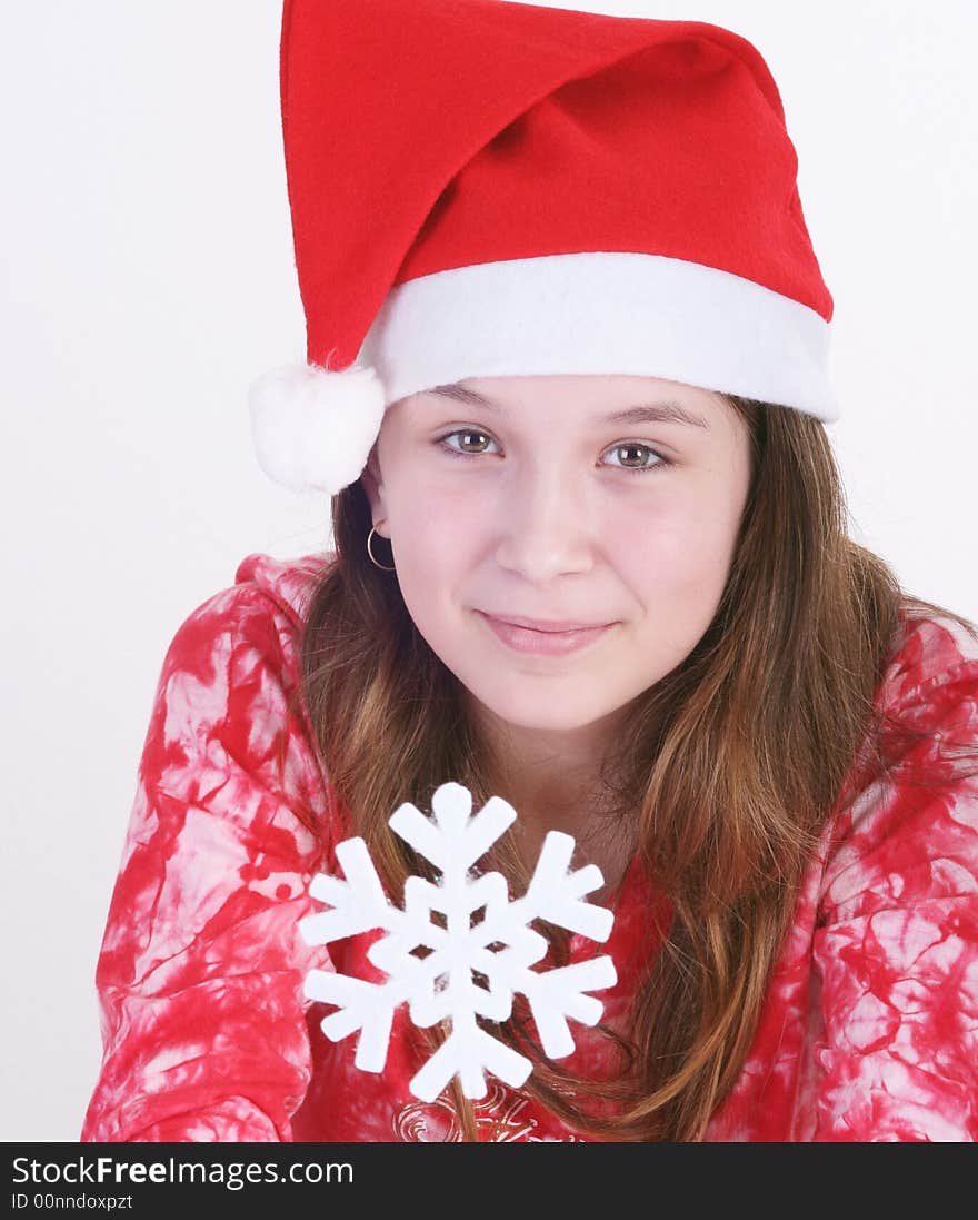 A portrait of a young teenager wearing a red Santa hat and red print top, holds out a large white snowflake in both hands in this studio setting. White background. A portrait of a young teenager wearing a red Santa hat and red print top, holds out a large white snowflake in both hands in this studio setting. White background.