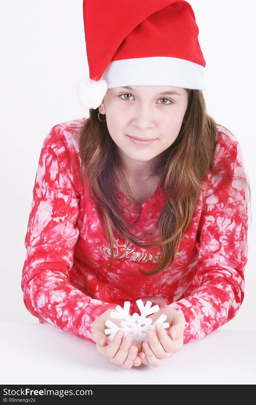 A portrait of a young teenager wearing a red Santa hat and red print top, holds out a large white snowflake in both hands in this studio setting. White background. A portrait of a young teenager wearing a red Santa hat and red print top, holds out a large white snowflake in both hands in this studio setting. White background.