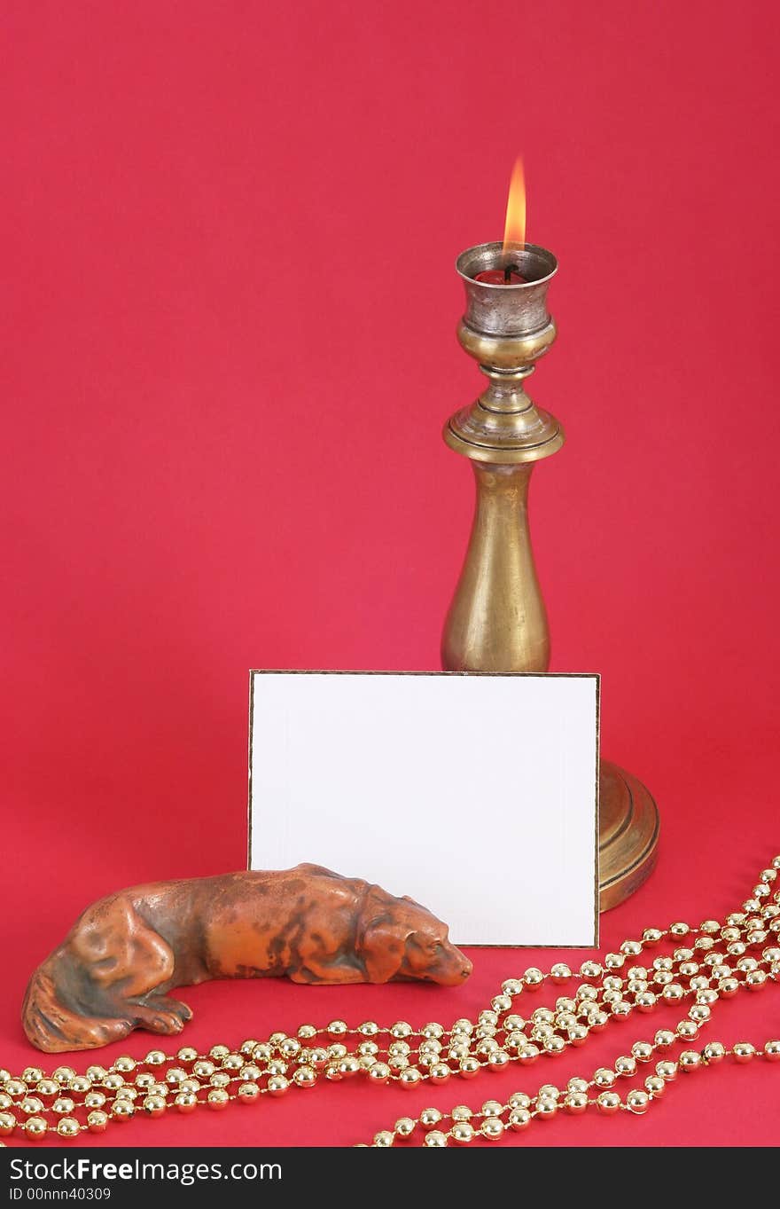 Christmas candle with flame. A white card in front. Red background.