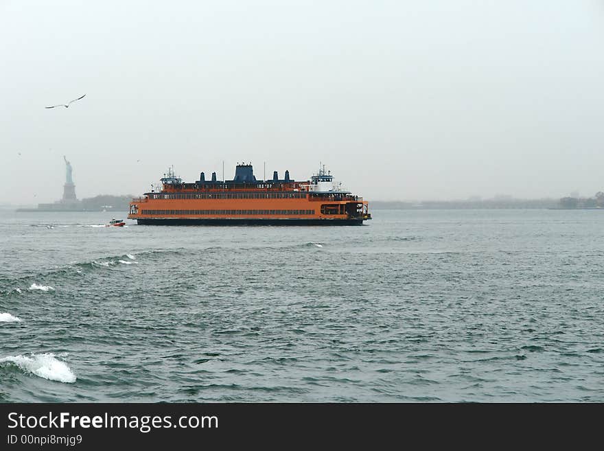 A picture of an Orange Ship in the New York Habor with statue of Liberty in distance background. A picture of an Orange Ship in the New York Habor with statue of Liberty in distance background