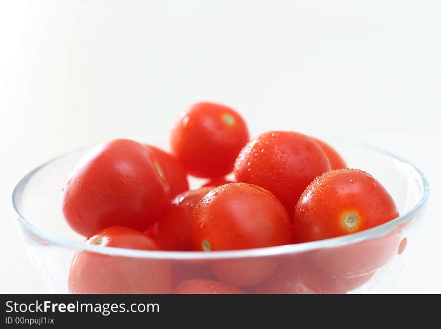 Cherry tomatoes in a transparent glass bowl on a white table-top