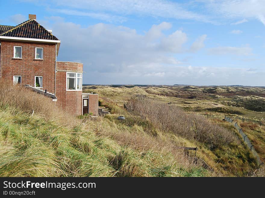 Dunes with house and grass situated in Zandvoort Holland. Wide view angle. On the background blue sky and clouds. Various colors of green.