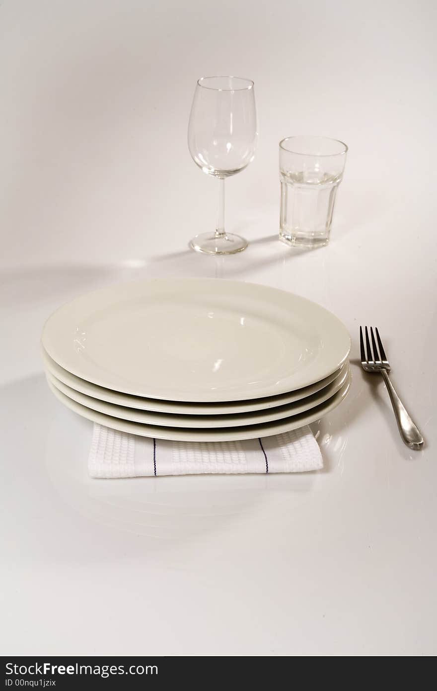 Table setting of four stacked classic plates , napkin , silver fork, wines glass and glass cup. Table setting of four stacked classic plates , napkin , silver fork, wines glass and glass cup.