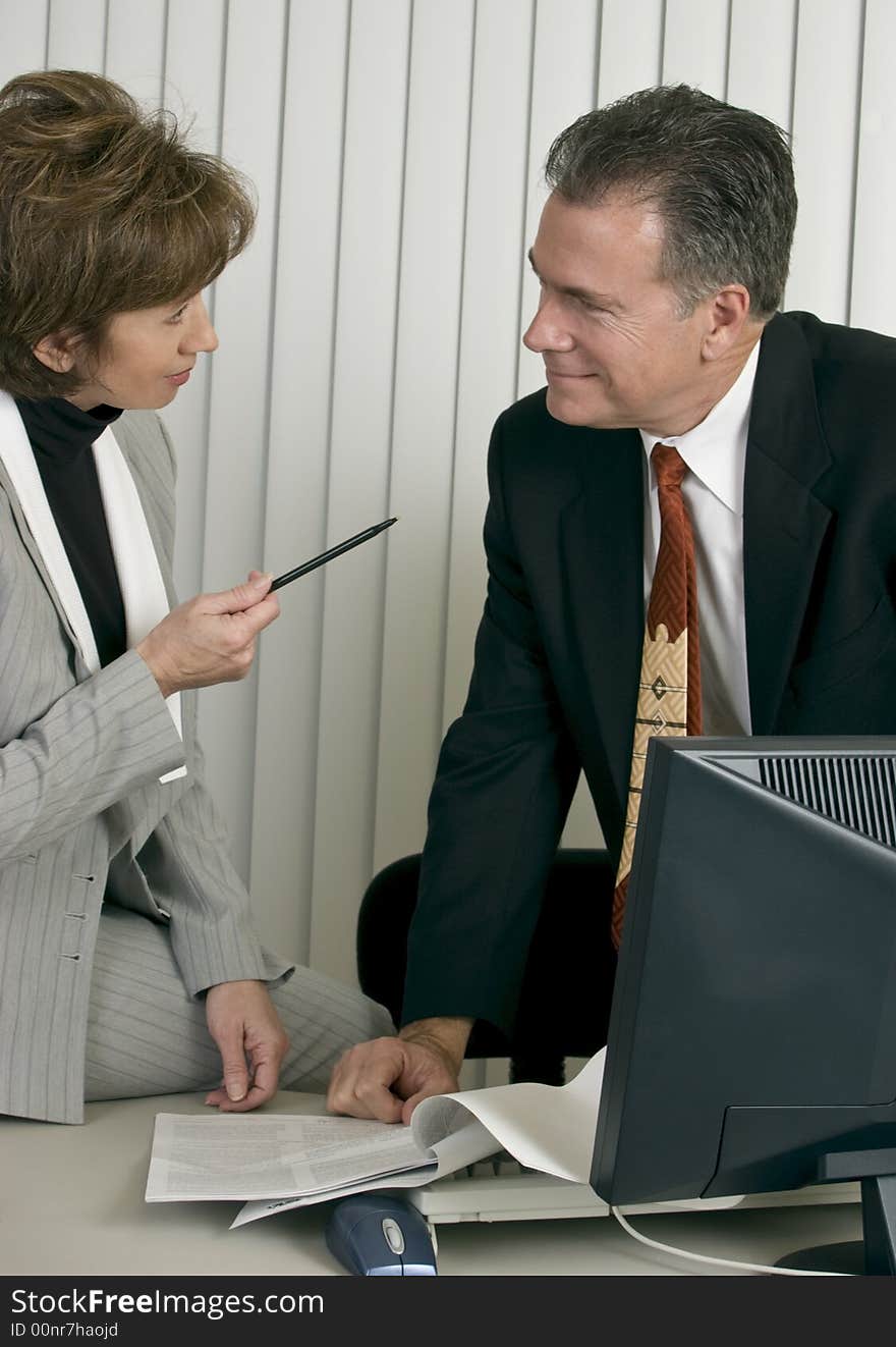 A man and a woman in an office setting appearing to be co-workers engaged in discussion. A man and a woman in an office setting appearing to be co-workers engaged in discussion.