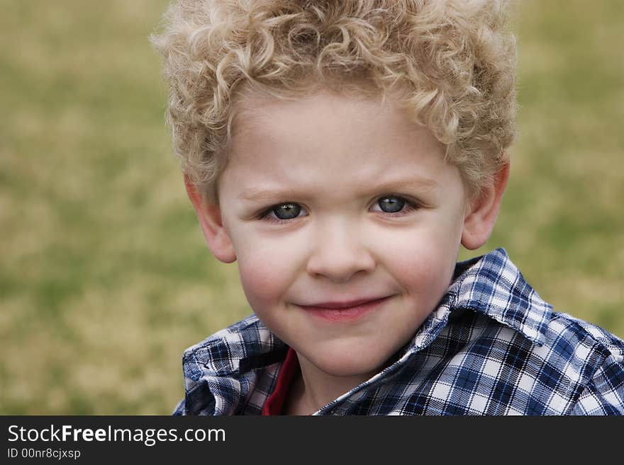 Smiling young boy in a plaid shirt with grass in the background. Smiling young boy in a plaid shirt with grass in the background