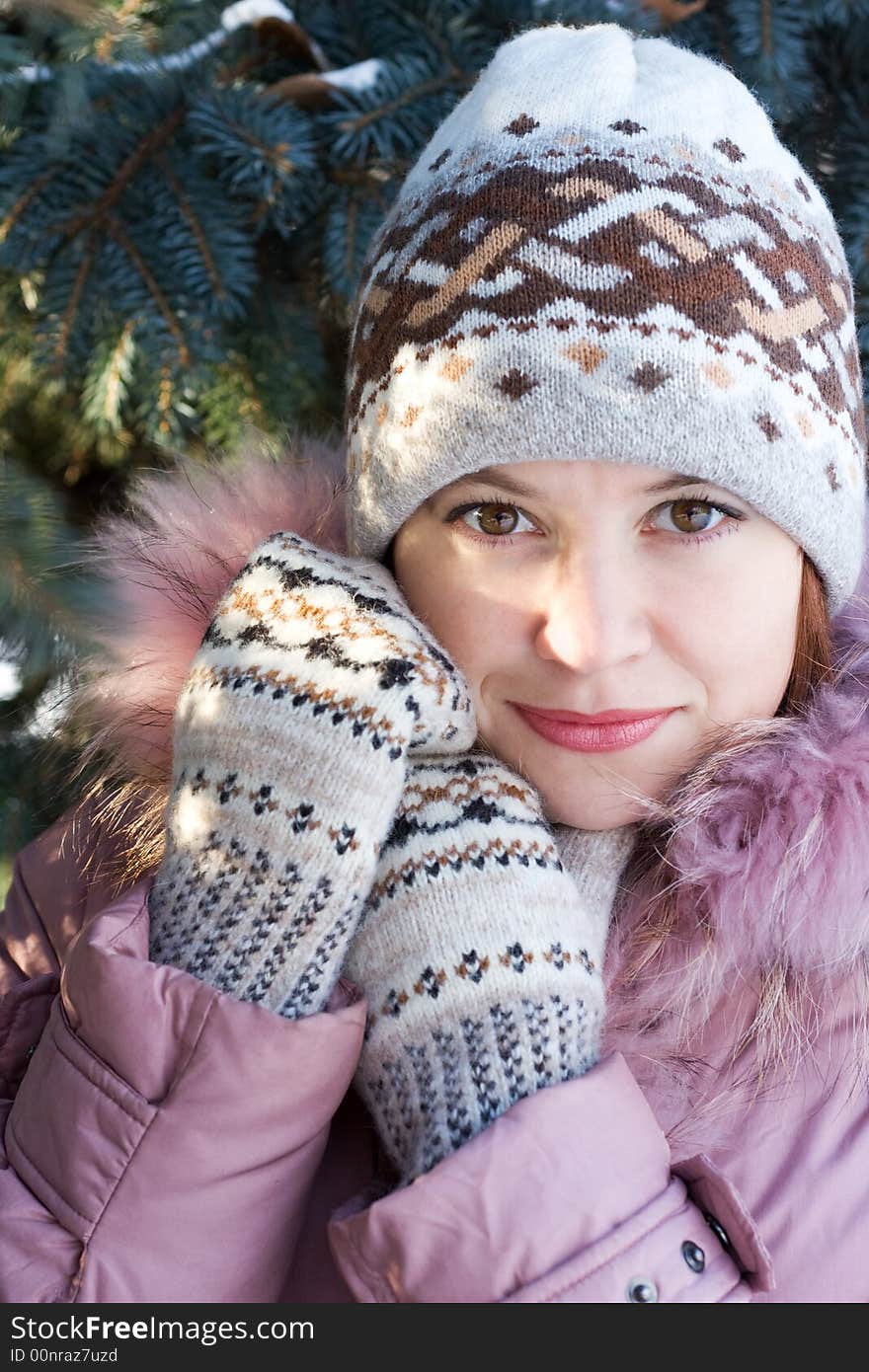 Beautiful girl in hat and mittens in snow-covered evergreens and rays of sun. Beautiful girl in hat and mittens in snow-covered evergreens and rays of sun