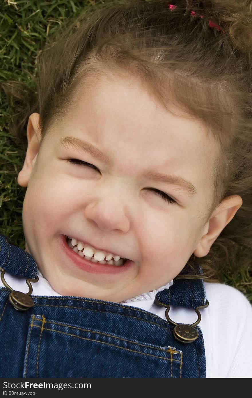 Little girl laying in the grass making a silly face with a big smile. Little girl laying in the grass making a silly face with a big smile.