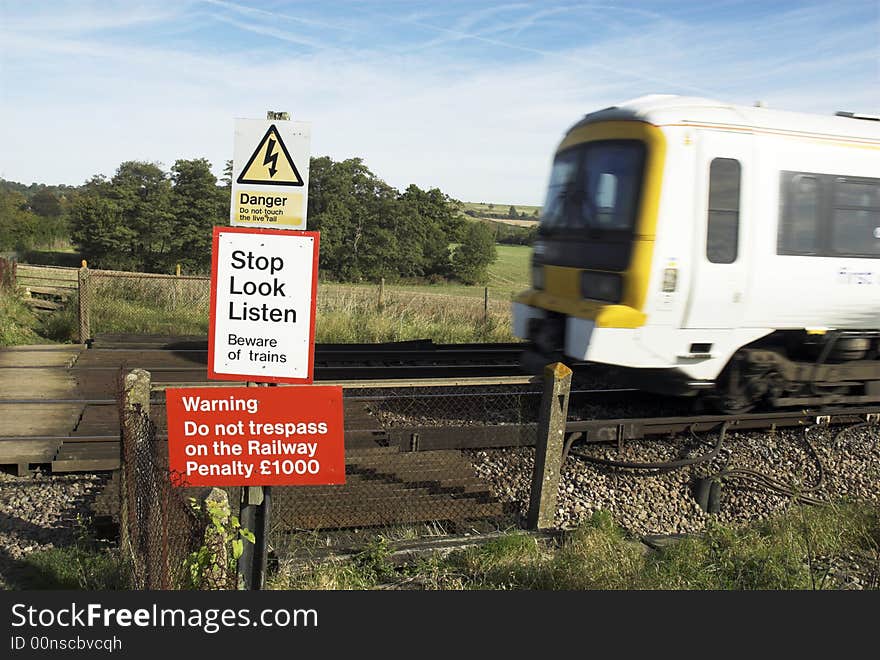 Fast train approaching railway pedestrian crossing, at which multiple warning signs are displayed.