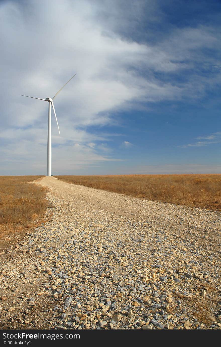 A gravel road leads up to a large white wind turbine. A gravel road leads up to a large white wind turbine.