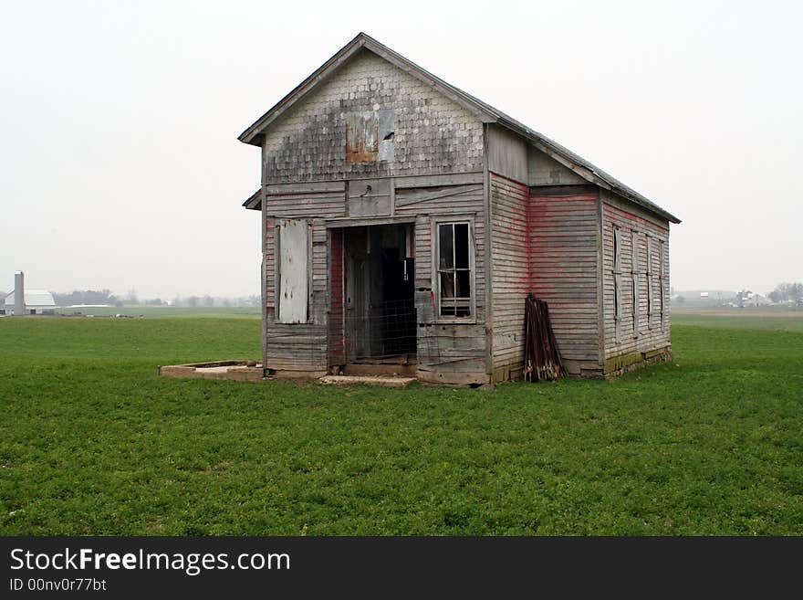 An old one room school house in a field on a cloudy day.