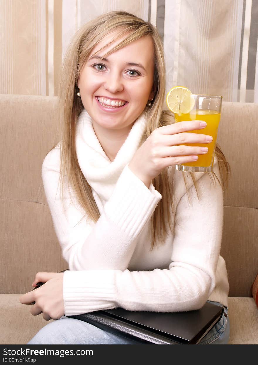 Smiling young woman after work on the couch with orange juice in hand. Smiling young woman after work on the couch with orange juice in hand.