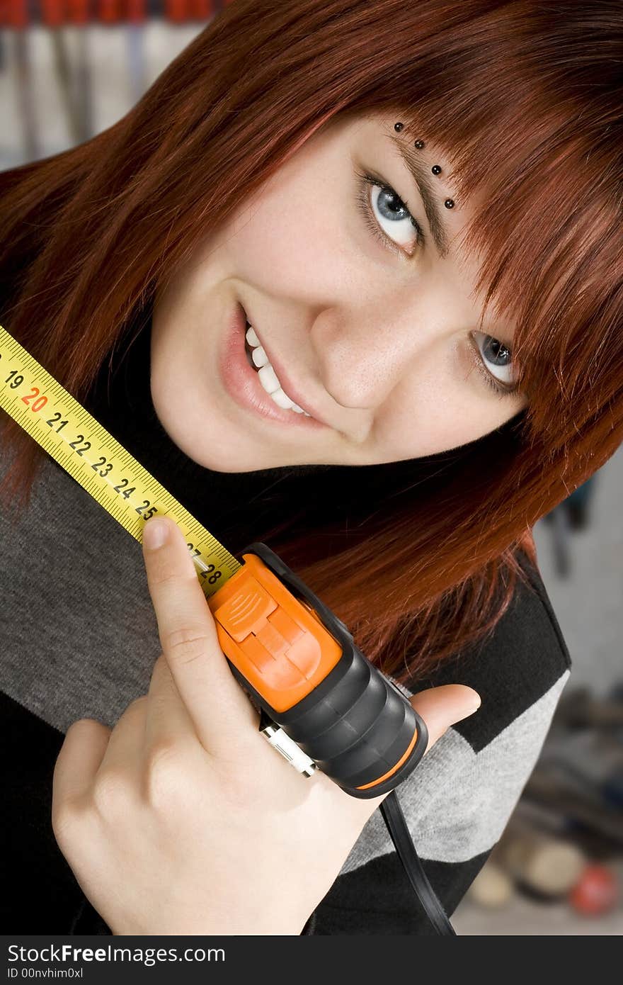 Beautiful redhead girl using measuring tape in workshop and pointing at 25cm.Studio shot.