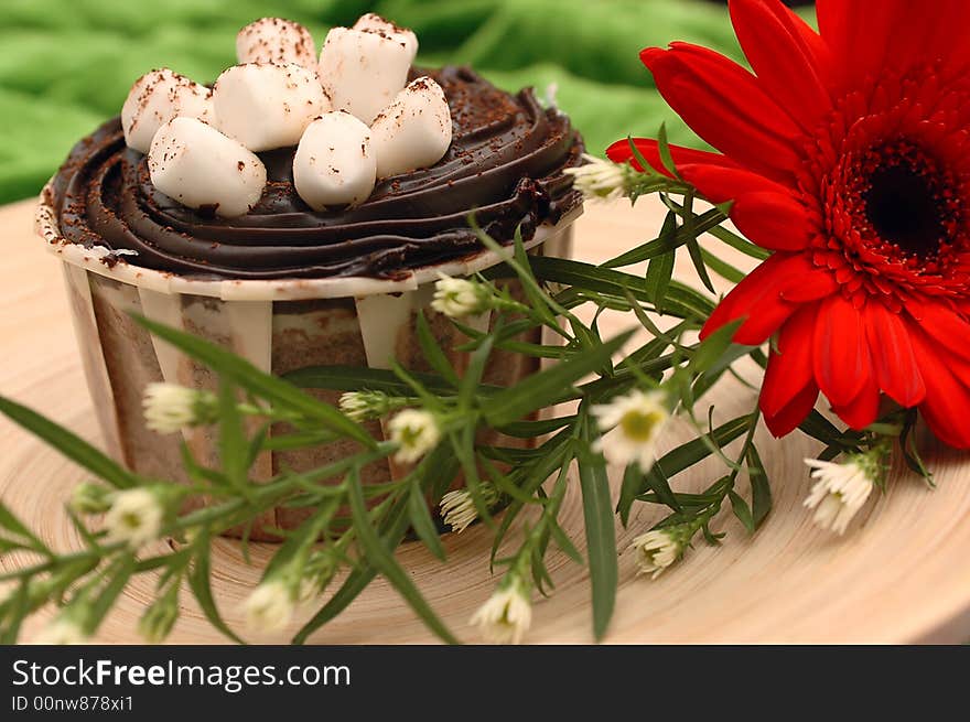 A chocolate cup cake with marshmallow toppings decorated with a red daisy. A chocolate cup cake with marshmallow toppings decorated with a red daisy