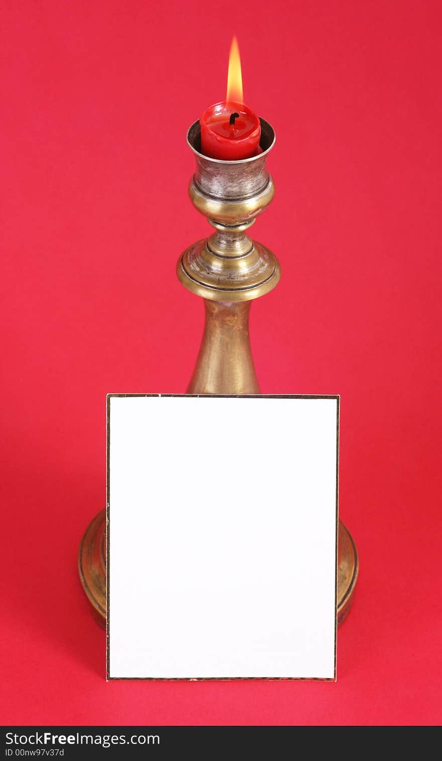 Christmas candle with flame.A white card in front.Red background. Christmas candle with flame.A white card in front.Red background.