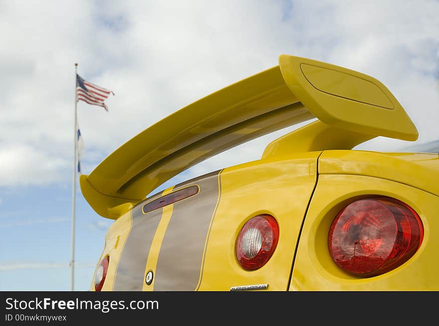 Tail end of a fast supercharged sports car with an American flag on a pole behind. Tail end of a fast supercharged sports car with an American flag on a pole behind