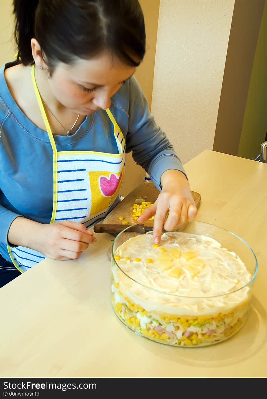 Woman garnishes layer salad in glass utensil. Woman garnishes layer salad in glass utensil