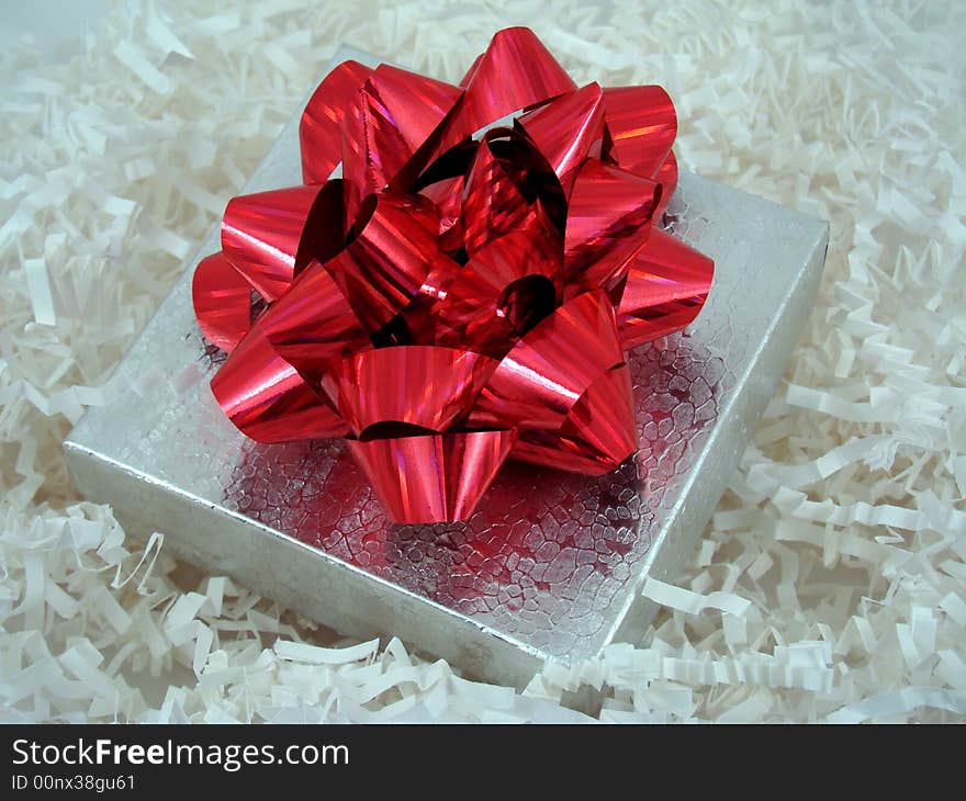 A present in a silver box with a red ribbon on top.