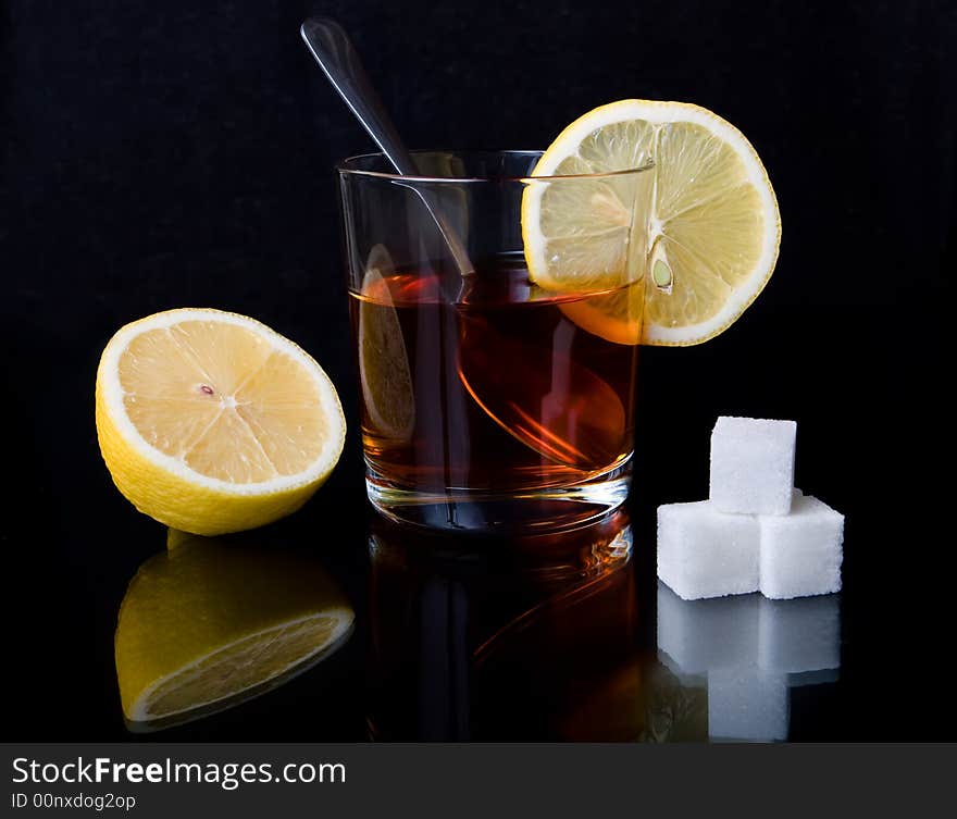 Glass with tea, the spoon, sugar and a lemon on a black reflecting surface. Glass with tea, the spoon, sugar and a lemon on a black reflecting surface