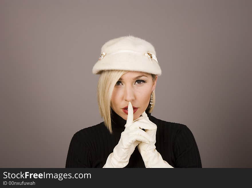 A blonde fashion model in white hat and gloves saying hush. A blonde fashion model in white hat and gloves saying hush