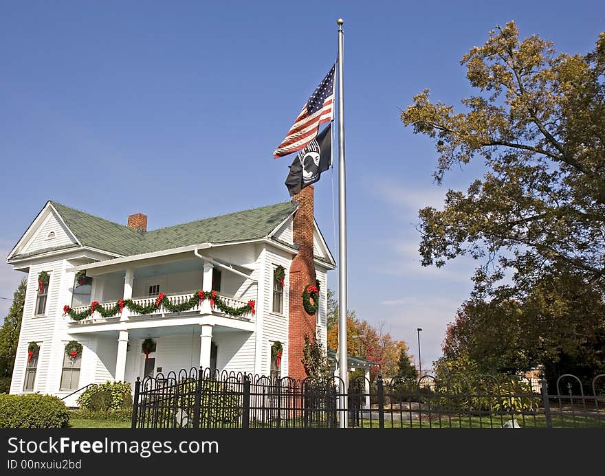 An old white colonial home decorated for Christmas with American flag and POW flag in front. An old white colonial home decorated for Christmas with American flag and POW flag in front