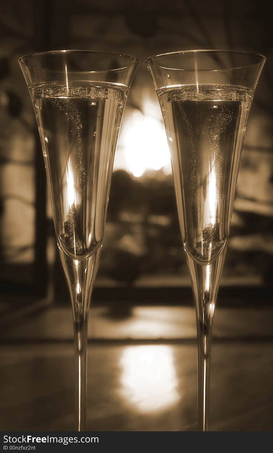 Two glasses of bubbly champagne by the fireplace. Sepia tone, selective focus. Two glasses of bubbly champagne by the fireplace. Sepia tone, selective focus.