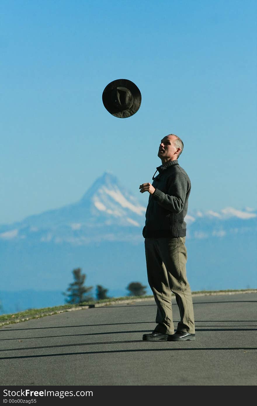 A man tosses a hat into the air, in front of a chain of mountains. A man tosses a hat into the air, in front of a chain of mountains.