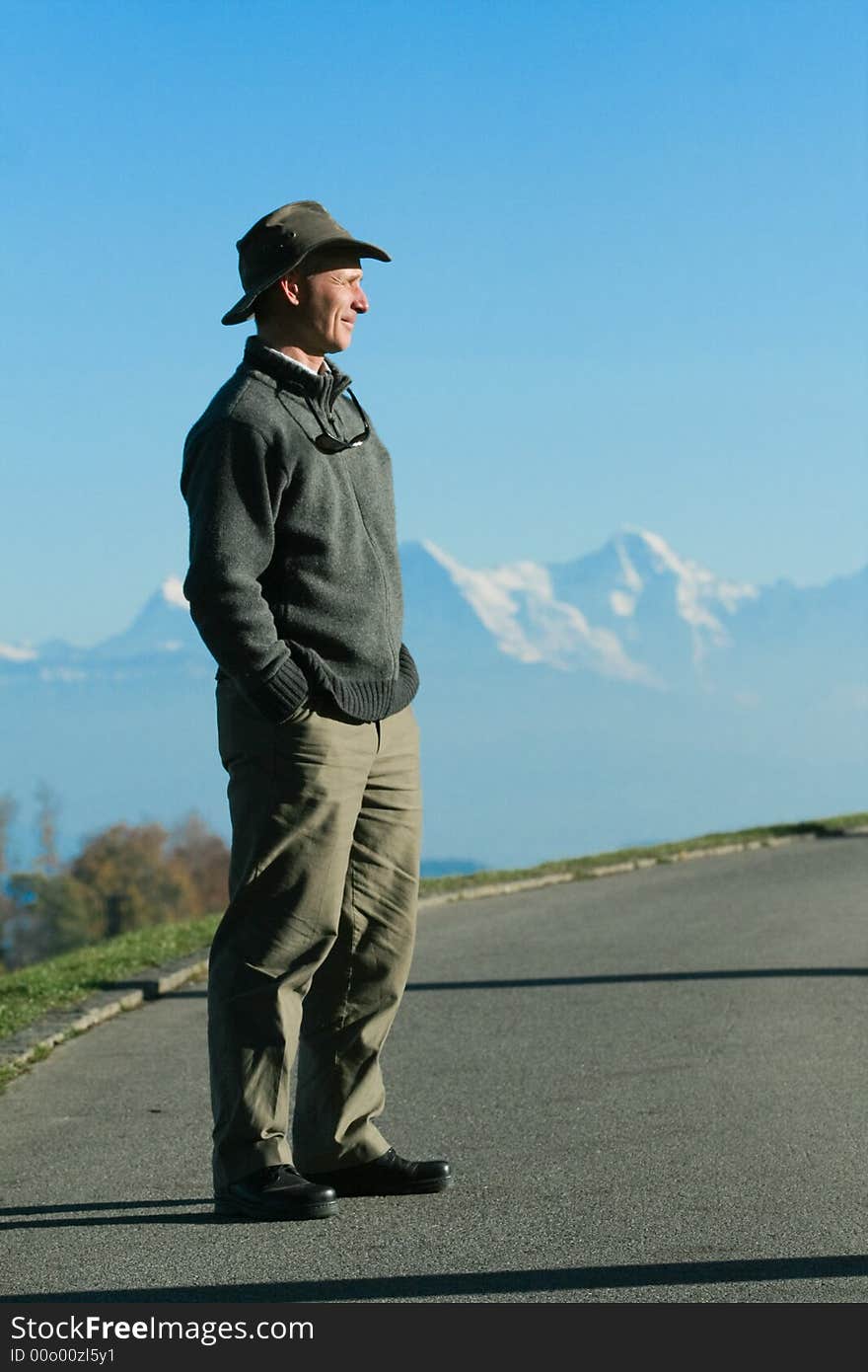 A man smiles as stands, hands in his pockets, surveying the horizon, in front of a chain of mountains in the Fall. A man smiles as stands, hands in his pockets, surveying the horizon, in front of a chain of mountains in the Fall.